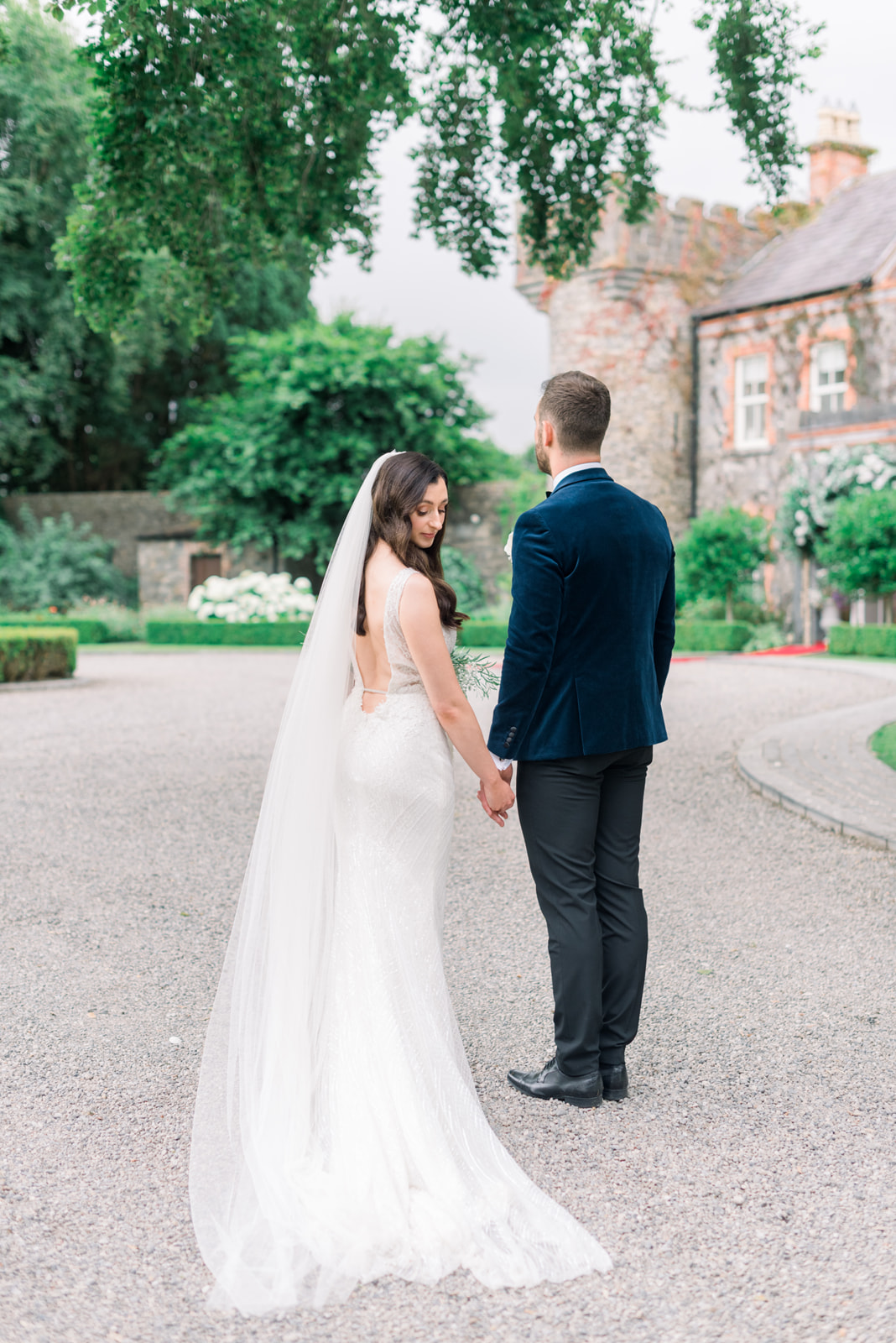 Bride's long veil and groom in velvet jacket facing the manor at Ballymagarvey Village